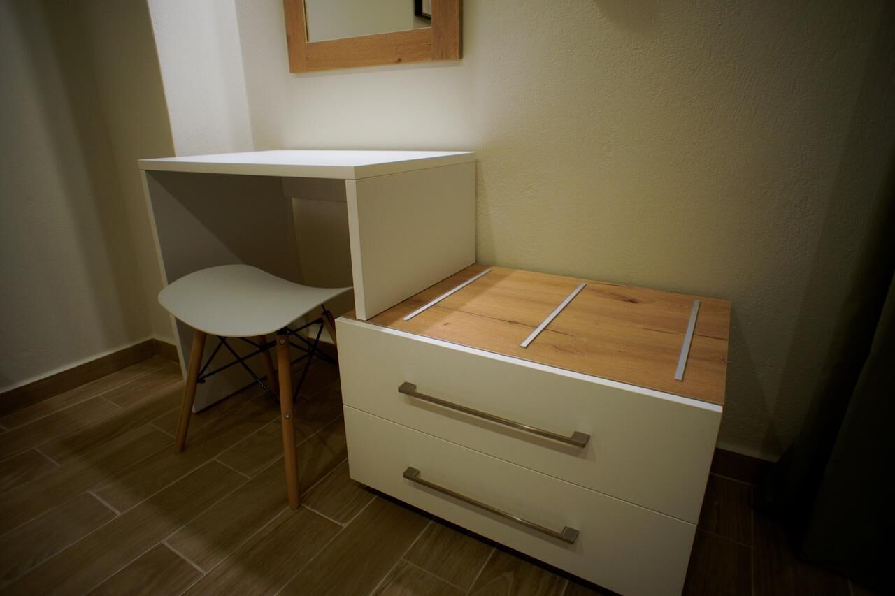 Una habitación pequeña con un escritorio blanco, una silla y una pequeña cómoda.