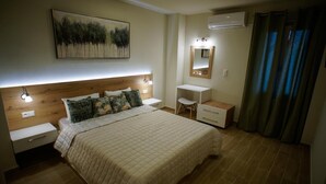 A bedroom with a large bed, bedside tables, a desk, a chair, a mirror, and a painting on the wall. - Sandika Apartments (Hersonissos)