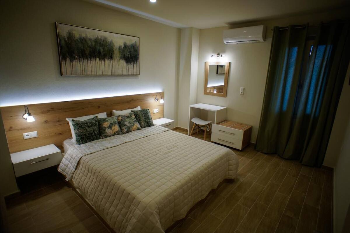 A bedroom with a large bed, bedside tables, a desk, a chair, a mirror, and a painting on the wall.