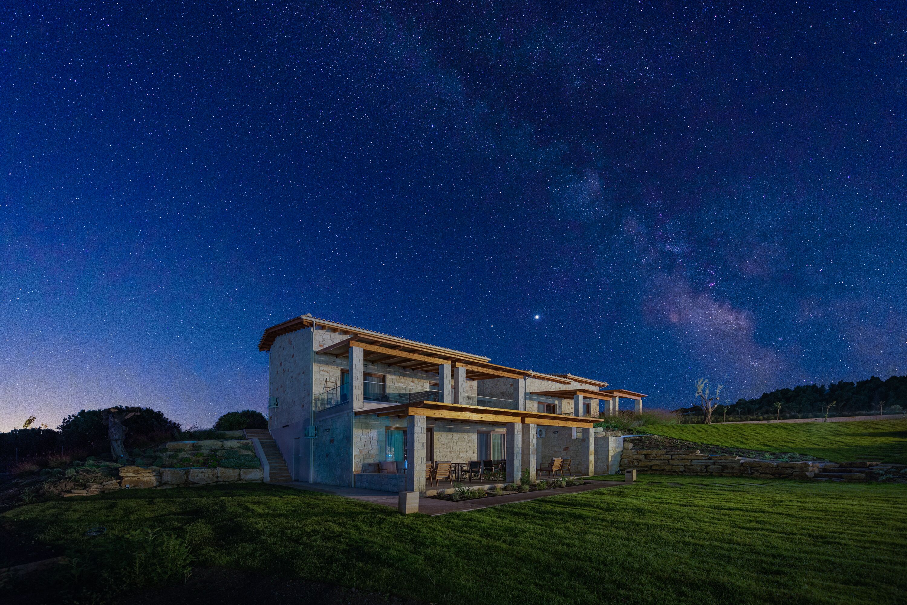 Una casa moderna con un amplio patio abierto, fachada de piedra y vista al cielo nocturno.