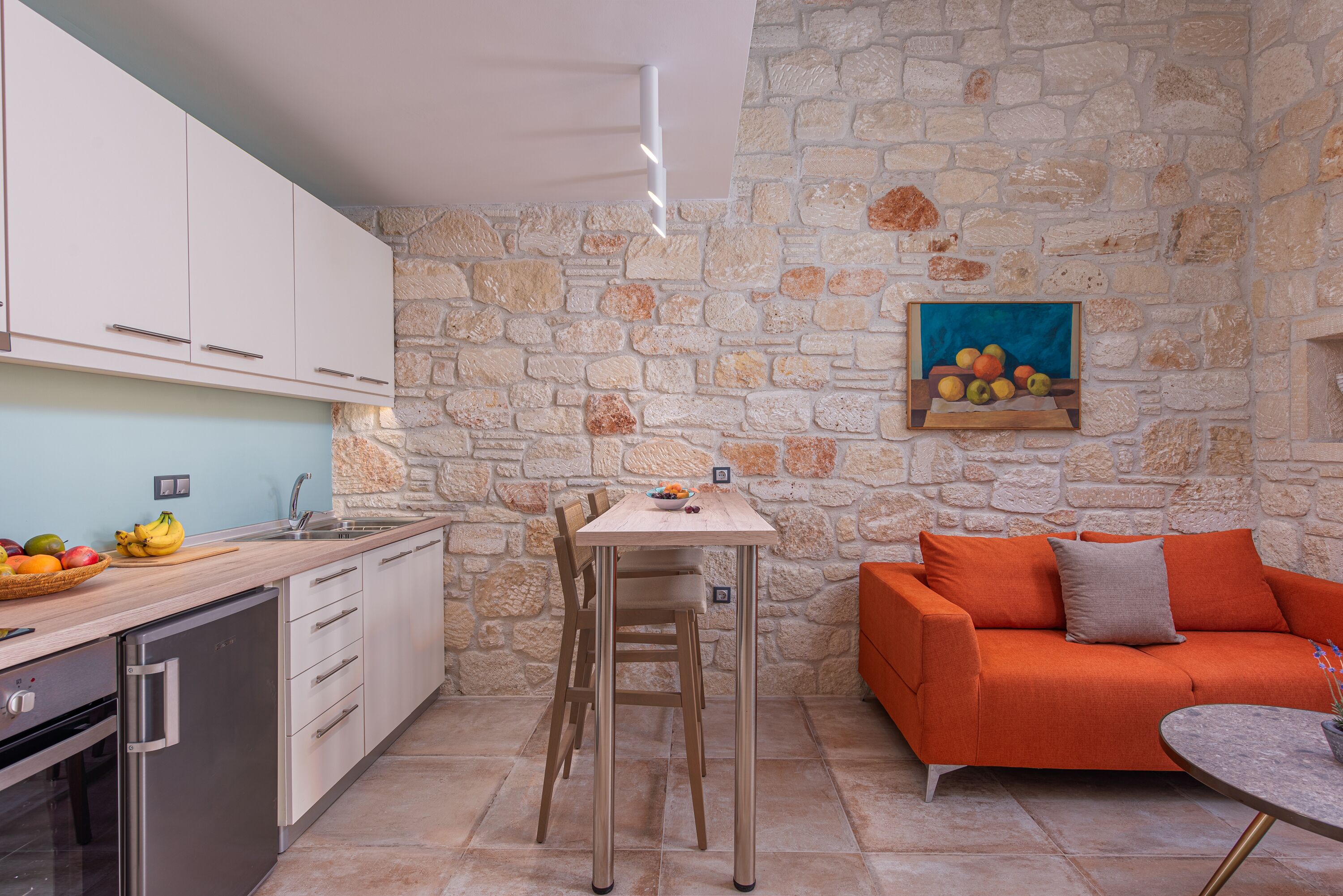 A compact kitchen with a stone wall, a dining table, and a sofa.