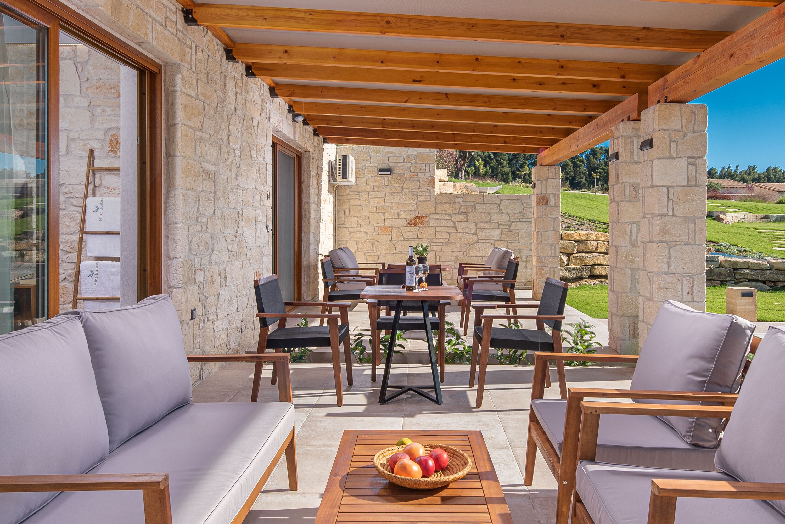 An outdoor patio with stone walls, wooden furniture, and a table with fruit.