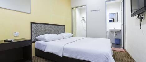 Habitación de hotel con cama, escritorio, espejo, televisor y baño con ducha y lavamanos.