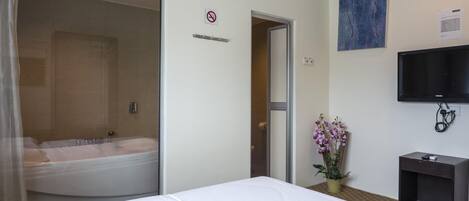A hotel room with a bed, a shower area, a television, and a no-smoking sign.