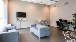 A modern office space with a grey sofa, a flat-screen TV, a desk with a computer, and a chair. - Raintree Hotel (Kuala Lumpur)