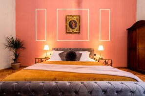 A bedroom with a large bed, two bedside tables with lamps, a potted plant, and a wooden wardrobe.