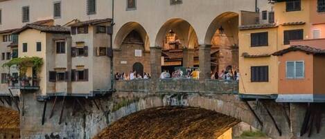 A stone bridge with arches spanning a calm river, surrounded by historic buildings with multiple windows and balconies.