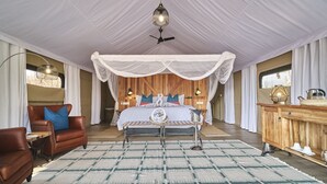 A bedroom with a canopy bed, wooden headboard, and a large window. - The Wallow Lodge (Victoria Falls)