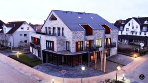 A modern multi-story building with a sloped roof, large windows, and balconies. - Störtebeker 4 (Kellenhusen)