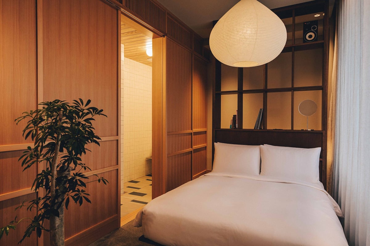 A hotel room with a large bed, wooden paneling, a potted plant, a ceiling light, and a radio.