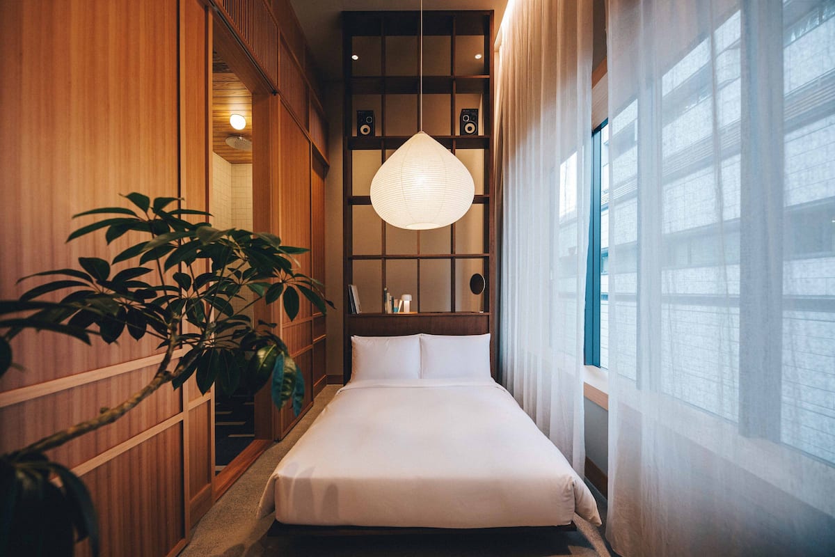 A hotel room with a bed, wooden paneling, a hanging light fixture, and a large window.