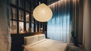 Una cama bien tendida con cabecera, un lámpara colgante y vistas a una ventana con cortinas.
