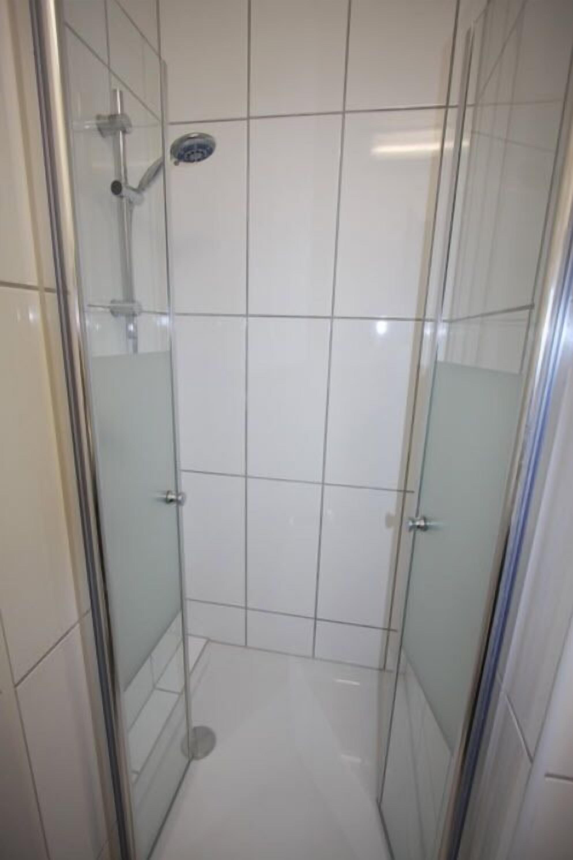 A glass-enclosed shower stall with a handheld showerhead and a wall-mounted control panel.