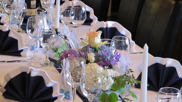Una mesa dispuesta para una ocasión formal con cristalería transparente, una vela blanca y centros de mesa florales.