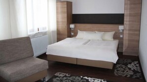 Un dormitorio con cama, sofá, armario y ventana con cortinas.