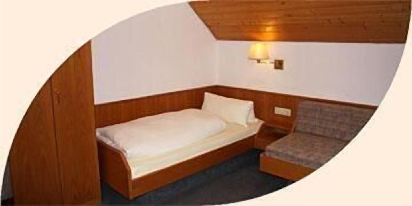 A small, single-bed room with wooden walls and a simple bed.