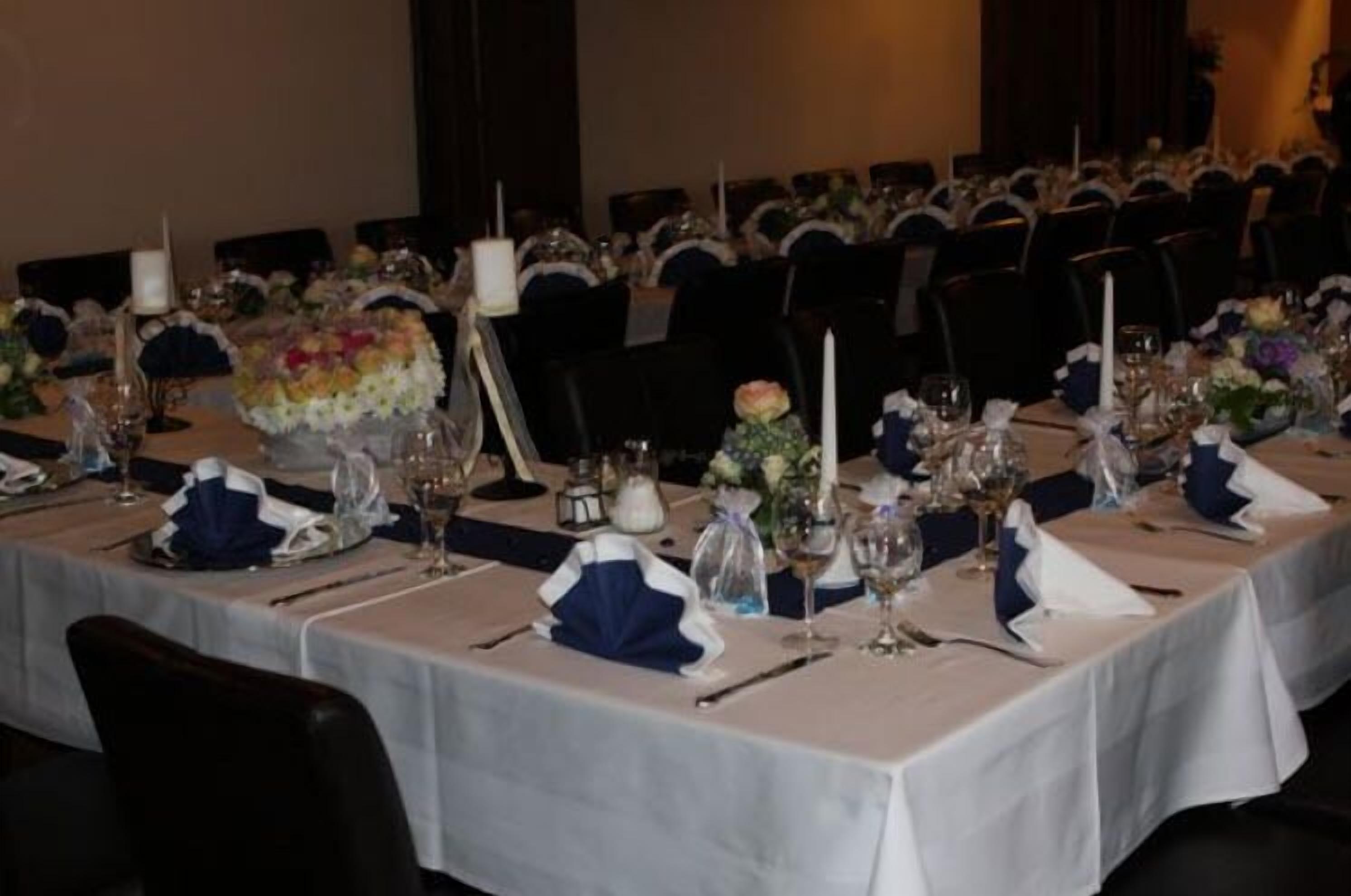 A banquet hall with tables set for a formal event, featuring white tablecloths, blue napkins, and floral centerpieces.