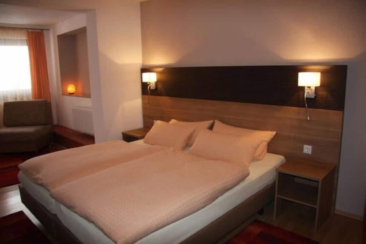 Una cama doble con cabecera de madera, dos lámparas de noche, una mesita de noche y una silla en una habitación de hotel.