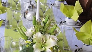 Una larga mesa de comedor con manteles verdes, vajilla blanca y centros de mesa florales.