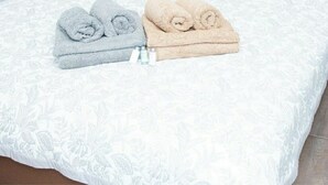 A neatly made bed with a white patterned bedspread and two rolled towels, one grey and one beige, placed on top.