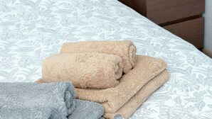 A neatly made bed with a patterned bedspread, a small wooden nightstand with a potted plant, and two folded towels.