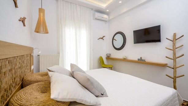 A modern hotel room with a bed, woven ottoman, wall-mounted TV, and a wooden headboard. - Beach Connection Naxos town (Naxos)