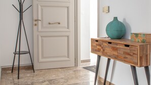 A hallway with a white door, a coat rack, a wooden console table with a vase, and a wall clock. - Beach Connection Naxos town (Naxos)