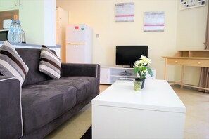 A living room with a grey sofa, a white coffee table with a potted plant, a flat-screen TV, and a wooden side table. - Bright furnished studio near metro in Tecom - ALIA (Dubai)