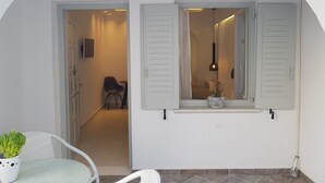 A white-walled room with a doorway leading to another room, a small table with a chair, and a potted plant. - Exclusive Studios Naxos Town (Naxos)