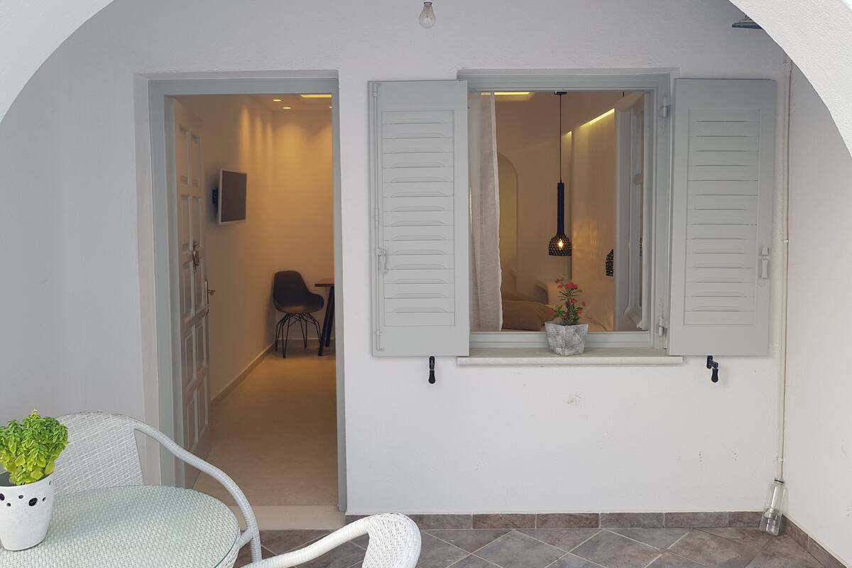 A white-walled room with a doorway leading to another room, a small table with a chair, and a potted plant.