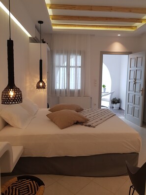 Un dormitorio moderno con una cama grande, dos lámparas colgantes, un radiador blanco y vistas al exterior a través de una ventana con cortinas blancas.
