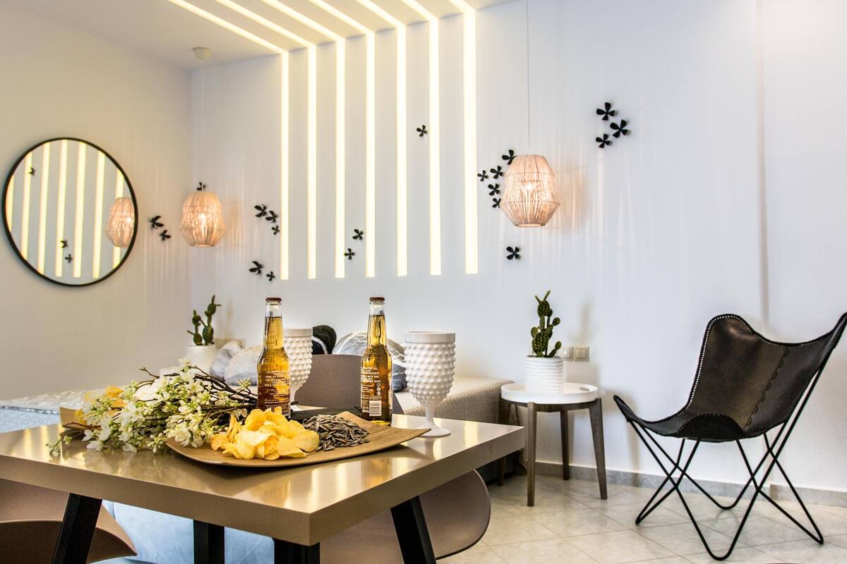 A modern dining area with a wooden table set for two, featuring a bottle of wine, a glass, and a floral arrangement.