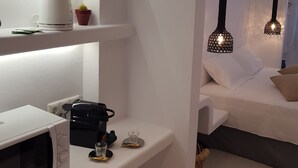 A modern, minimalist room with a white color scheme, featuring a microwave, a kettle, a small cactus, and a glass on a shelf. There is a bed with white bedding and two hanging pendant lights. - Exclusive Studios Naxos Town (Naxos)