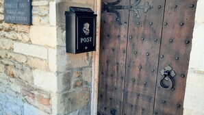 Een houten deur met een metalen brievenbus en een klopper op de muur, met daarop de tekst 'POST'.