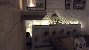 Een gezellige woonkamer met een stenen muur, een witte console tafel met een decoratief modelhuis, sfeerverlichting en een gestreept kussen op een bank.