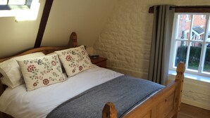 Een houten bed met bloemenkussens, een grijze deken en een nachtkastje met een afstandsbediening.