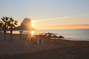 A beach with a large rock formation, palm trees, and beach chairs. - Cosy Second Sea Line Apart - Exclusive Residence (Calpe)