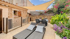 Un pati amb seients de relaxació, una taula i cadires, tot envoltat d'una paret de pedra i plantes.