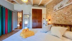 Habitació d'hotel amb llit, una porta de fusta, mur de pedra i cortina colorida.