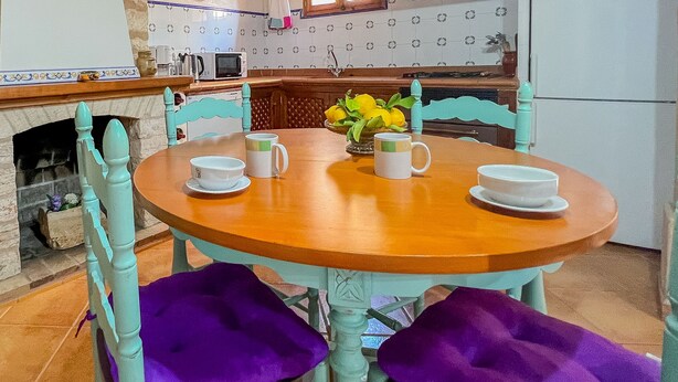 A dining area with a round wooden table, four chairs with purple cushions, and a vase with yellow flowers. - Charming Villa Can Xesquet (Felanitx)