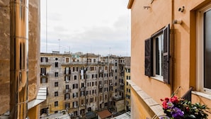 A narrow street view with buildings on either side, a balcony with flowers, and a clear sky.