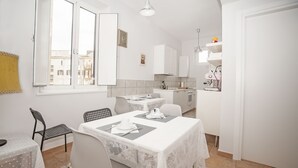 A compact kitchen with white cabinets, a dining table set with a white tablecloth, and a patterned rug.