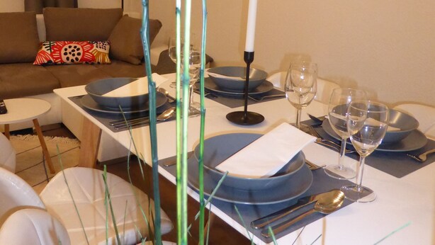A dining area with a white table set for two, featuring blue plates, silverware, and a white candle centerpiece. - Apartment Goethe (Jena)
