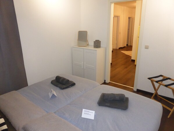 A bedroom with a bed, a small desk, a wardrobe, and a wooden chair.