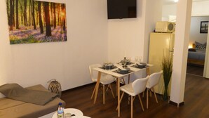 A dining area with a table set for four, a flat-screen TV mounted on the wall, and a painting of a forest scene. - Apartment Goethe (Jena)
