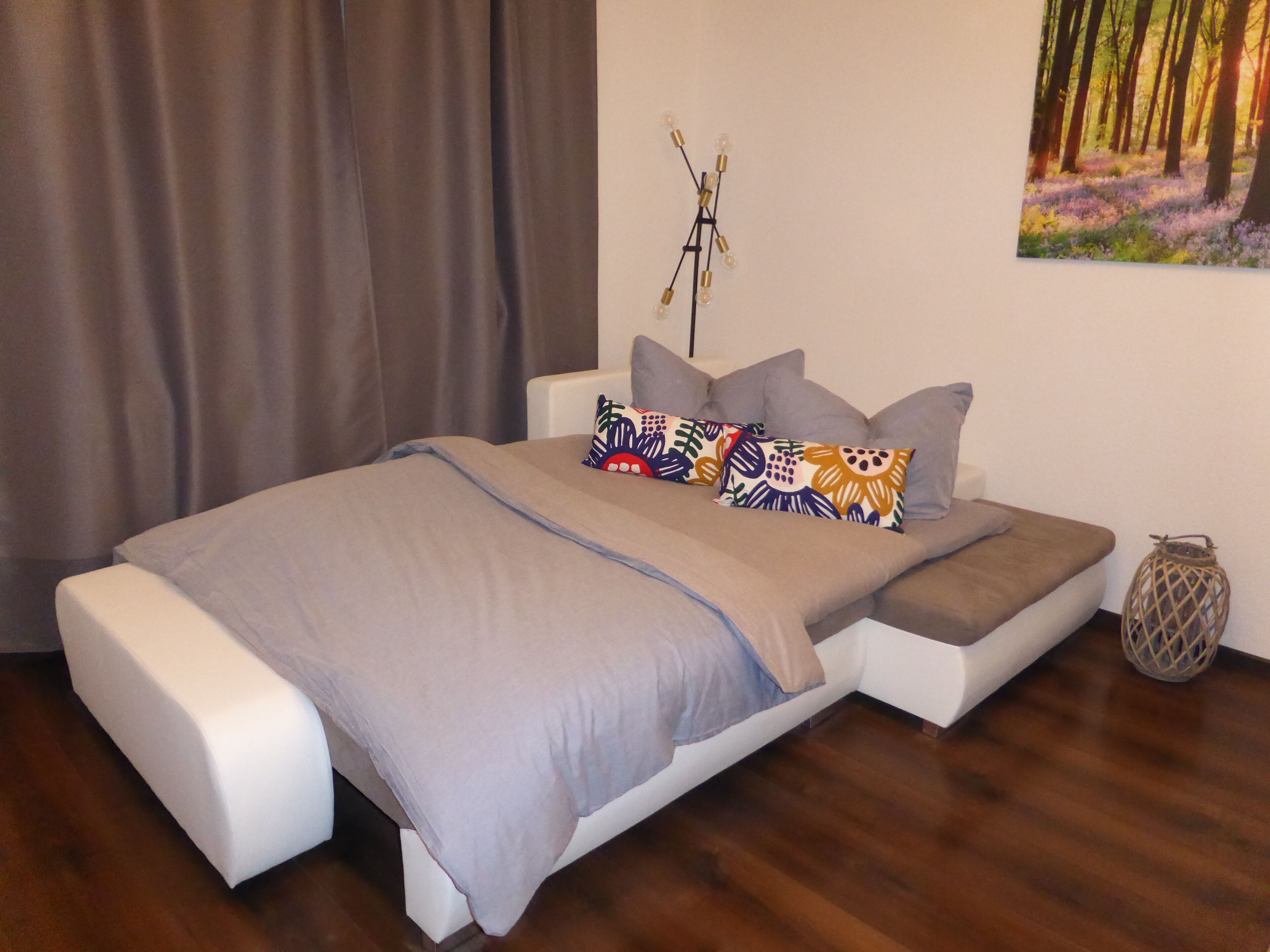 Ein modernes Schlafzimmer mit einem Bett, Kissen, einer Wandleuchte und einem Waldgemälde.