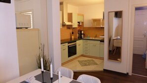 A modern kitchen with white cabinets, a built-in oven, and a coffee maker. There is a dining area with a table, chairs, and candles. - Apartment Goethe (Jena)