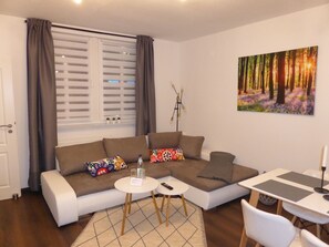 A modern living room with a sectional sofa, a small round table, and a dining table. - Apartment Goethe (Jena)