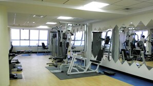 Un gimnasio con diversas máquinas de ejercicio, ventanas amplias y piso de madera.