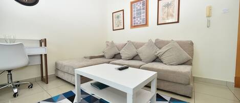 Una sala de estar con un sofá blanco, una mesita de centro blanca, un escritorio con una silla y un tapete estampado.